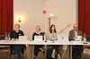 Vier Personen diskutieren an einem Tisch mit Laptops und Mikrofonen in einem Saal.