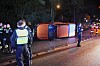 Rettungskräfte sichern nachts ein umgestürztes orangefarbenes Fahrzeug auf einer Straße.