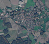 Luftaufnahme einer Ortschaft mit Häusern, Straßen und Feldern in ländlicher Umgebung.