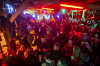 Tanzende Gäste feiern bei rotem Licht in einem vollen Club; über der Menge glitzert eine Discokugel.