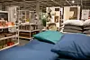 Blau bezogenes Bett mit Kissen vor Regalen in einem Einrichtungshaus