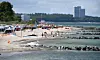 Badegäste, Boote und Wellen an einem Sandstrand vor bewaldeter Küste und Hochhäusern