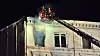 Feuerwehrleute arbeiten nachts mit einer Drehleiter an der Fassade eines historischen Gebäudes.