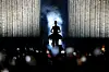 Céline Dion steht silhouettenhaft auf der Bühne der Plenitude Arena in Nanterre vor blau beleuchteten Vorhängen.