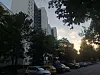 Sonnenuntergang zwischen Hochhäusern, Bäumen und einer von Autos gesäumten Straße.