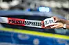 Ein Absperrband wird vor einem Polizeiwagen ausgerollt, an dem das Blaulicht leuchtet. (Symbolbild)