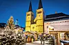 Verschneiter Weihnachtsmarkt mit Tannenbaum, Menschen und beleuchteter Stadtkirche bei Nacht