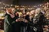 Gruppe warm gekleideter Menschen stößt auf einem festlich beleuchteten Wintermarkt an.