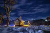 Beleuchtete Kapelle in verschneiter Berglandschaft unter einem wolkigen Nachthimmel