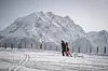 Zwei Skifahrer vor einem verschneiten Bergmassiv auf einem schneebedeckten Hang