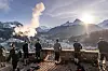 Wanderer beobachten eine Dampfwolke vor schneebedeckten Bergen im Sonnenlicht.