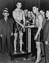 Joe Louis und Max Schmeling beim Wiegen 1936, flankiert von Joe Jacobs und weiteren Beobachtern.