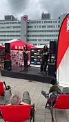 Sängerin und Techniker auf einer Open-Air-Bühne, dahinter ein Bürogebäude und sitzende Zuschauer