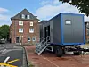 Blauer Containeranhänger mit Treppe vor einem Backsteingebäude an einer Straße