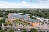 Luftaufnahme eines Einkaufszentrums mit orangefarbenen Gebäuden, Parkplätzen, Straßen und viel Grün.