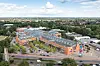 Luftaufnahme eines Einkaufszentrums mit orangefarbenen Gebäuden, Parkplätzen, Straßen und viel Grün.