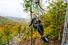 Person schwebt beim Seilrutschen durch einen herbstlichen Wald mit Kletterelementen.