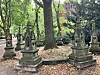Ornamentierte historische Grabmale stehen zwischen Bäumen auf einem parkähnlichen Friedhof.