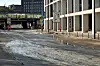 Breite verschmutzte Innenstadtstraße mit Hochhäusern, Haltestelle und gelbem Nahverkehrsfahrzeug im Hintergrund