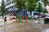 Einsatzkräfte stehen an einer überfluteten Straße in Hamburg, während Wasser aus einem Keller gepumpt wird.