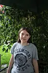 Mädchen mit grauem T-Shirt steht in einem grünen Garten unter dichtem Blattwerk.