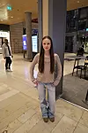 Junge Frau steht in einer hellen Passage vor einer Säule, im Hintergrund Menschen, Anzeigetafeln und Sitzplätze.