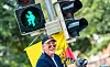 Otto Waalkes lächelt neben einer Ampel mit türkisfarbenem Otto-Symbol unter gelbem Schirm.