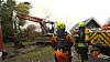 Feuerwehrleute sichern in Bunsoh ein Brandgelände, während ein Bagger Trümmer eines Reetdachhauses räumt.