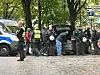 Uniformierte Einsatzkräfte stehen neben einem schwarzen Wagen und einem Polizeitransporter an einer bewaldeten Straße.