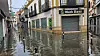 Überflutete Einkaufsstraße in Algeciras: Wasser steht vor Geschäften und spiegelt die Häuserfassaden.