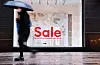 Eine Passantin mit Regenschirm geht am Schaufenster einer Modekette in der Innenstadt vorbei.