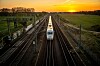 Zug auf der Bahnstrecke Berlin-Hamburg zwischen Gleisen und Oberleitungen bei Sonnenuntergang.