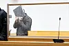 Ein Angeklagter mit Handschellen verdeckt sein Gesicht hinter einer Akte