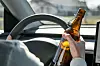 Eine Person sitzt am Steuer und hält eine Bierflasche in der Hand.