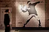 Ein Mitarbeiter betrachtet in der Ausstellung „The Mystery of Banksy – A Genius Mind“ in der ehemaligen Galeria Kaufhof das Wandbild mit dem Titel „Flower Thrower“