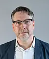 Bodo Mrozek in Hemd und Jacket. Er trägt eine Brille und hat gräuliches Haar.