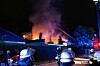 Einsatzkräfte der Feuerwehr stehen vor einem brennenden Haus.