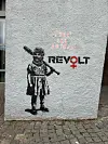 Ein Graffiti: Ein kleines Mädchen im Kleid hat eine Skimaske auf und einen Baseballschläger in der Hand. Neben ihr steht das Wort Revolt.