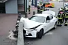 Ein weißer Maserati Ghibli steht mit zerdrückter Front an einer Mauer, im Hintergrund Feuerwehrleute und Polizisten