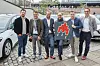 Sechs Männer vor Mietwagen halten ein Schild hoch