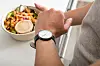 Mann schaut auf seine Uhr und hat einen Teller Essen in der anderen Hand.