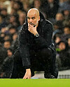 Pep Guardiola hockt auf dem Rasen und schaut nachdenklich.