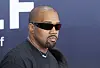 Kanye West mit schwarzer Sonnenbrille und schwarzem Oberteil vor einer dunklen Veranstaltungsrückwand