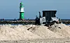 Große Sandhaufen werden am Ostseestrand von einer Planierraupe verteilt.