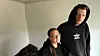 Ein Mann und eine Frau stehen vor einer weißen Wand, an der Risse zu sehen sind.
