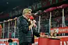 Michael Trippel spricht in ein Mikrofon. Im Hintergrund ist die Fankurve des 1. FC Köln zu sehen
