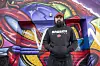 Jan Schütt steht auf dem Kiez vor einer Wand mit Graffiti